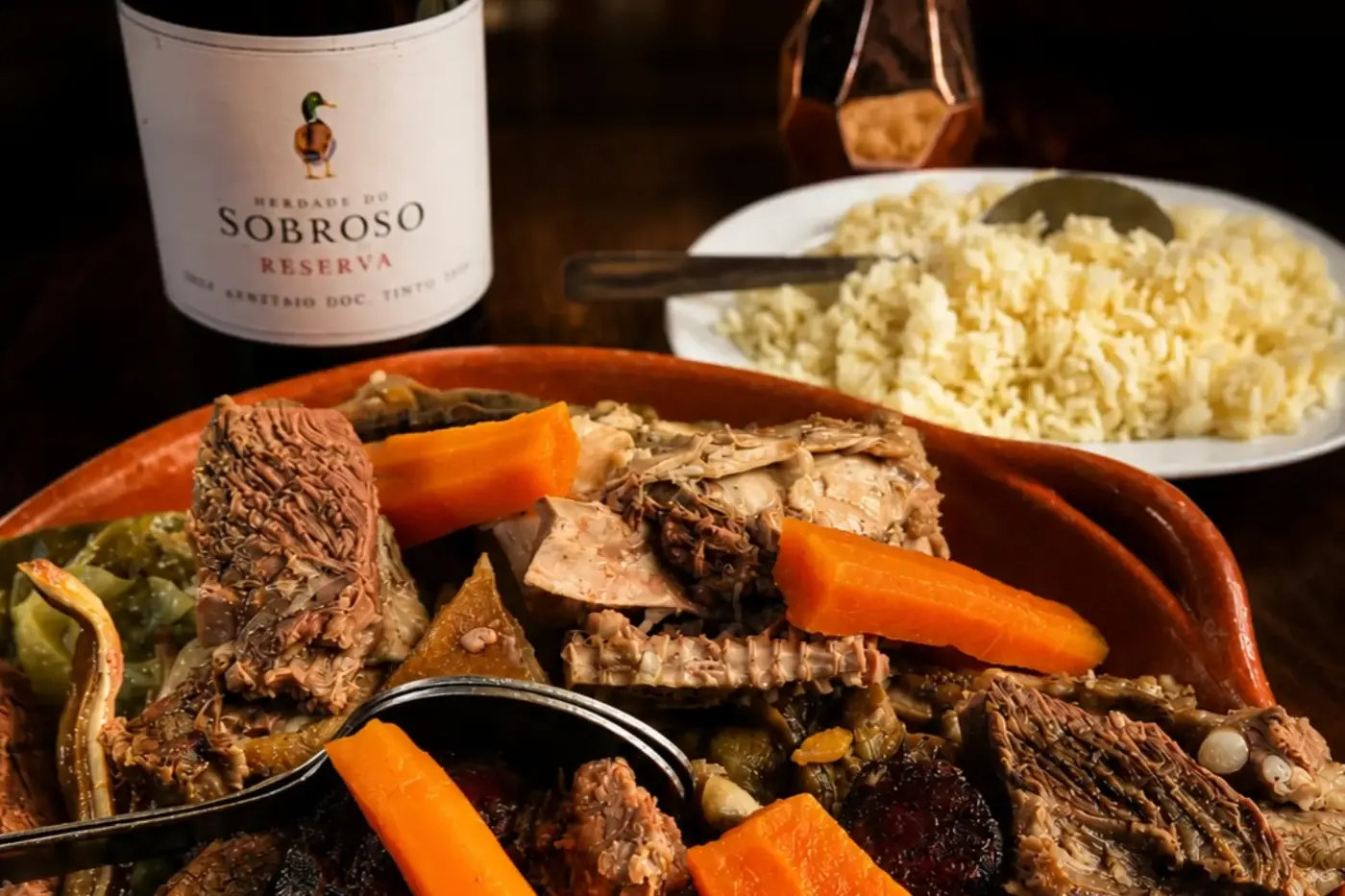Cozido à portuguesa num tacho de barro, com arroz, vinho tinto e flores na mesa